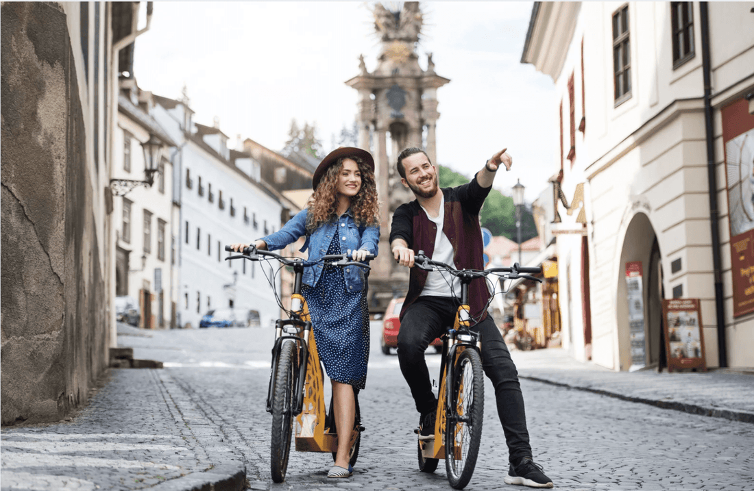 Two people with yellow electric bikes on a cobblestone street in a city setting, front view