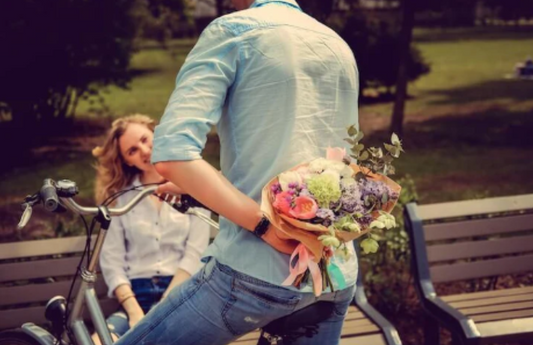 Man on e-bike hiding flower bouquet behind back, woman sitting on park bench, Pogo Cycles