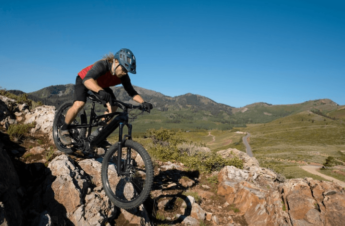 Mountain biker riding an electric bike on rocky trail with hills, Pogo Cycles e-bike