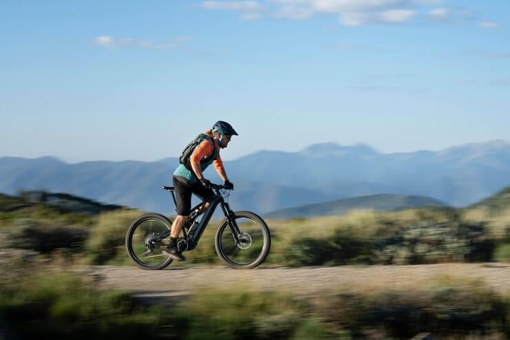 Electric mountain bike side view ridden on dirt trail with mountains in background