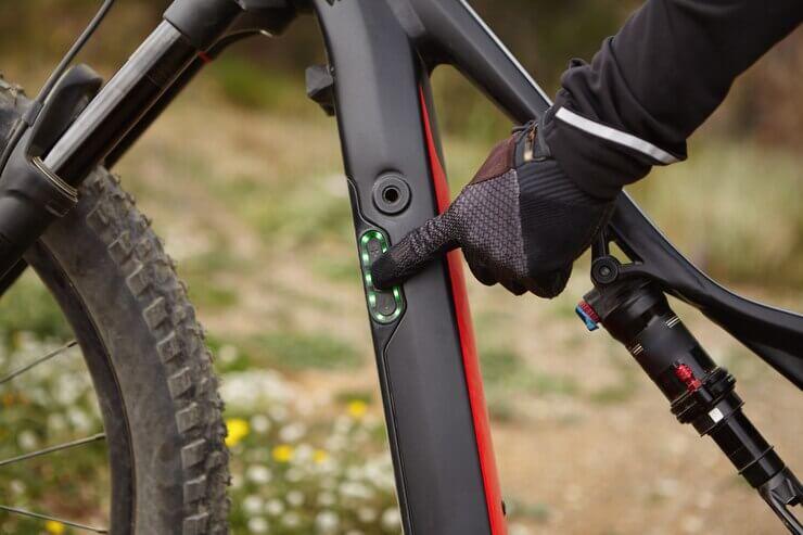 Close-up of electric mountain bike battery indicator being pressed, black and red frame