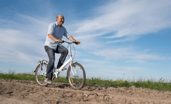White electric bike ridden by senior man on a dirt path, side view in outdoor setting