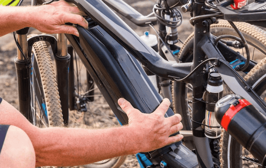 Hands installing a battery on a black electric bike with thick tires outdoors at Pogo Cycles