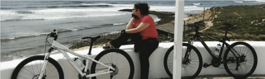 White and black electric bikes on a seaside wall with a person enjoying coastal view
